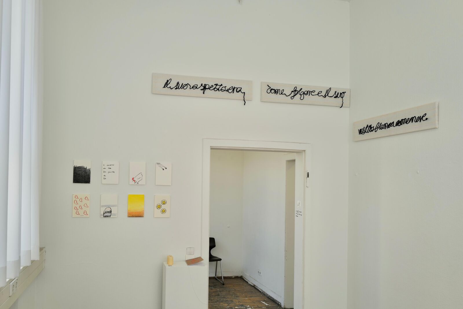 Installation view: three strips of monk’s cloth with handwriting in black wool above a doorway – ‘Il suo aspetto era / come folgore e il suo / vestito bianco come neve.’ – and small drawings on the wall beside it